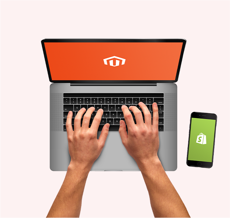 person working on laptop with Magento logo on screen. mobile phone to the side with Shopify logo.